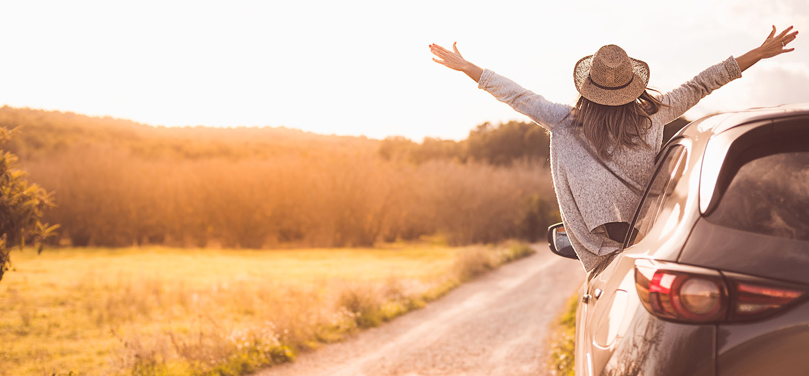 Happy girl celebrating success at sunset. The girl is wearing a hat and her arms are outstretched.