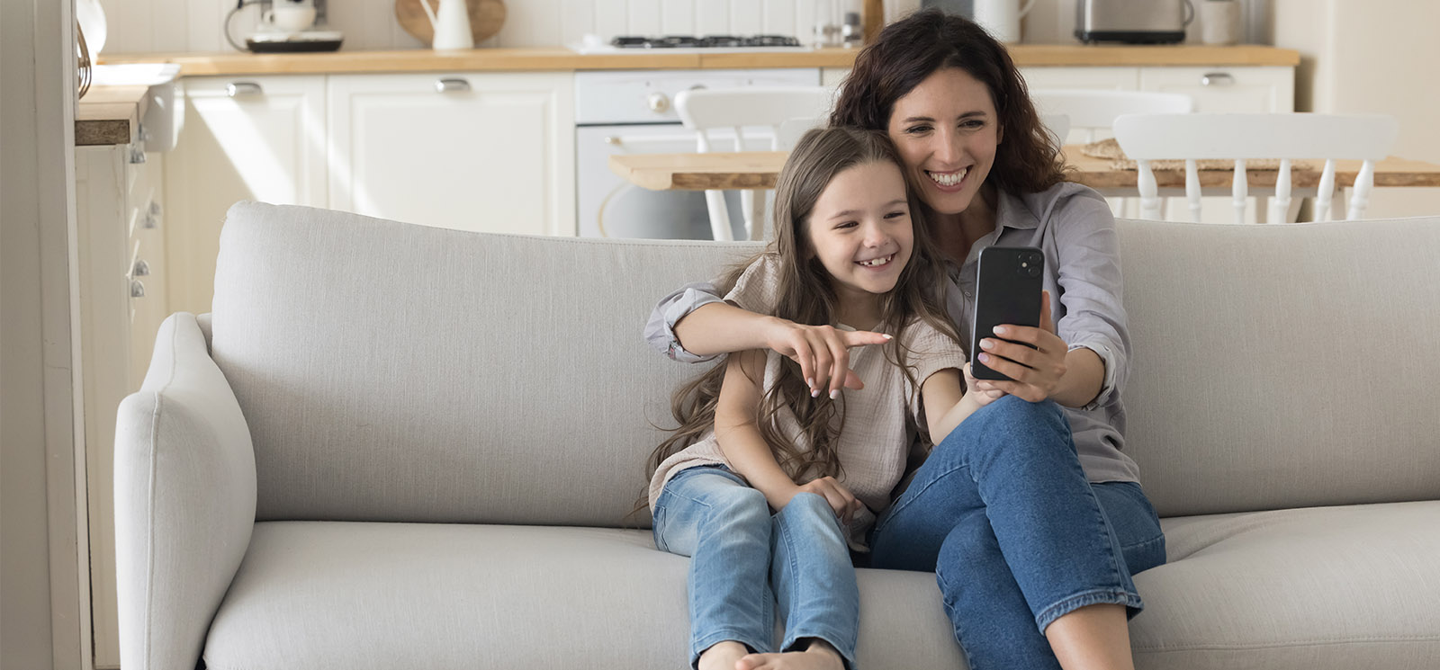 Cheerful mother hugging happy kid girl, using smartphone for Internet communication